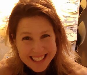 Selfie of lady in halterneck dress, smiling into camera. Behind a long table set for a dinner