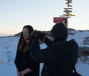 Man dressed as medieval lady with black cape and hood being filmed with close up on face