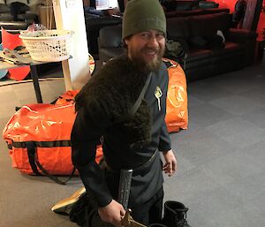 Man standing on knees dressed as a medieval lord holding sword, but wearing beanie