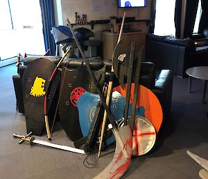 Collection of wooden shields, medieval weapons and bows and arrows leaning against back of leather couch