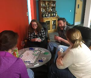 Group of four sitting around coffee table playing Sequence, a combined card and board game