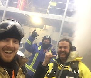 Selfie of three men in winter gear in store room which is filling with smoke