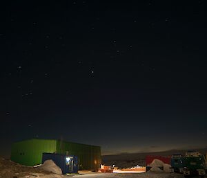 View looking across station at night to Green Store and Emergency Vehicle Store and in background ice plateau with light just coming up over the horizen