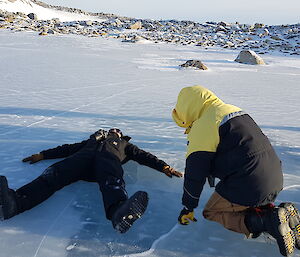 Man lies flat on his back on an ice lake while other expeditioners (3) look on