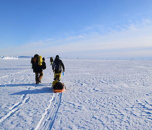Flat expanse of sea-ice with people walking across carrying pack and pullijng sled