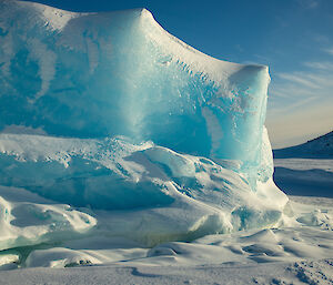 Close up of bright blue ice berg filling two thirds of picture, right third showing sea ice extending to rocky shoreline