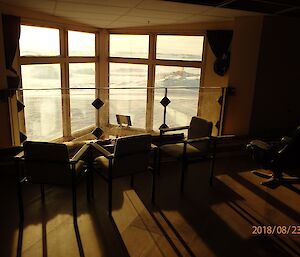 Floor area with seating facing out large windows at center top, beams of sun shining in and illuminating the chairs and floor