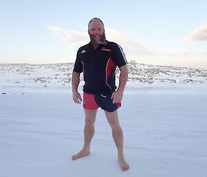 Man in shorts, canterbury crusaders t-shirt, and bare feet, stands out on the snow covered ground
