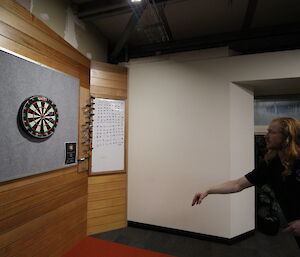 Darts board on left, man mid throw on right