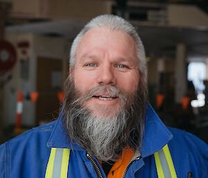 Headshot of man in blue jacket with hi-vis tape down chest, with full grey beard with lighter stripe at chin.