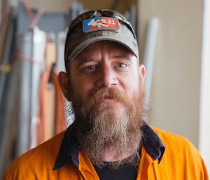 Headshot of man in hi-vis shirt with worn grey ball cap and auburn beard with grey around chin, which is a bit unkempt.