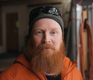 Headshot of man in orange hoodie, wearing green beanie, with fullsome red beard.