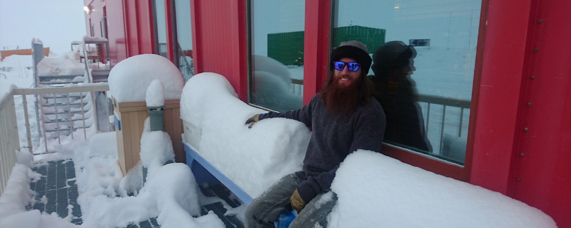 Man sits in centre of bench seat with mounds of snow to mid-chest height either side.
