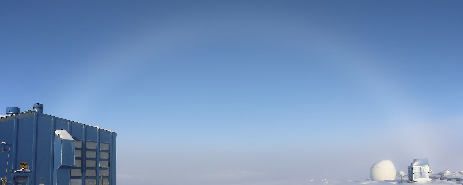 View across station buildings into fog over bay, above fog is a rainbow shape made of fog particles