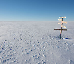 Flat featureless snow covered ground extends to the horizen, on right of picture is a wooden sign post with arrows pointing in a number of directions