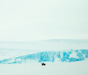 lone quad bike in the distance on sea-ice with blue ice cliffs rising behind
