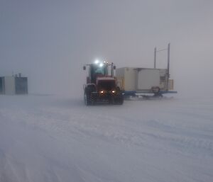 Tractor dragging generator van on sled into position, in whiteout conditions