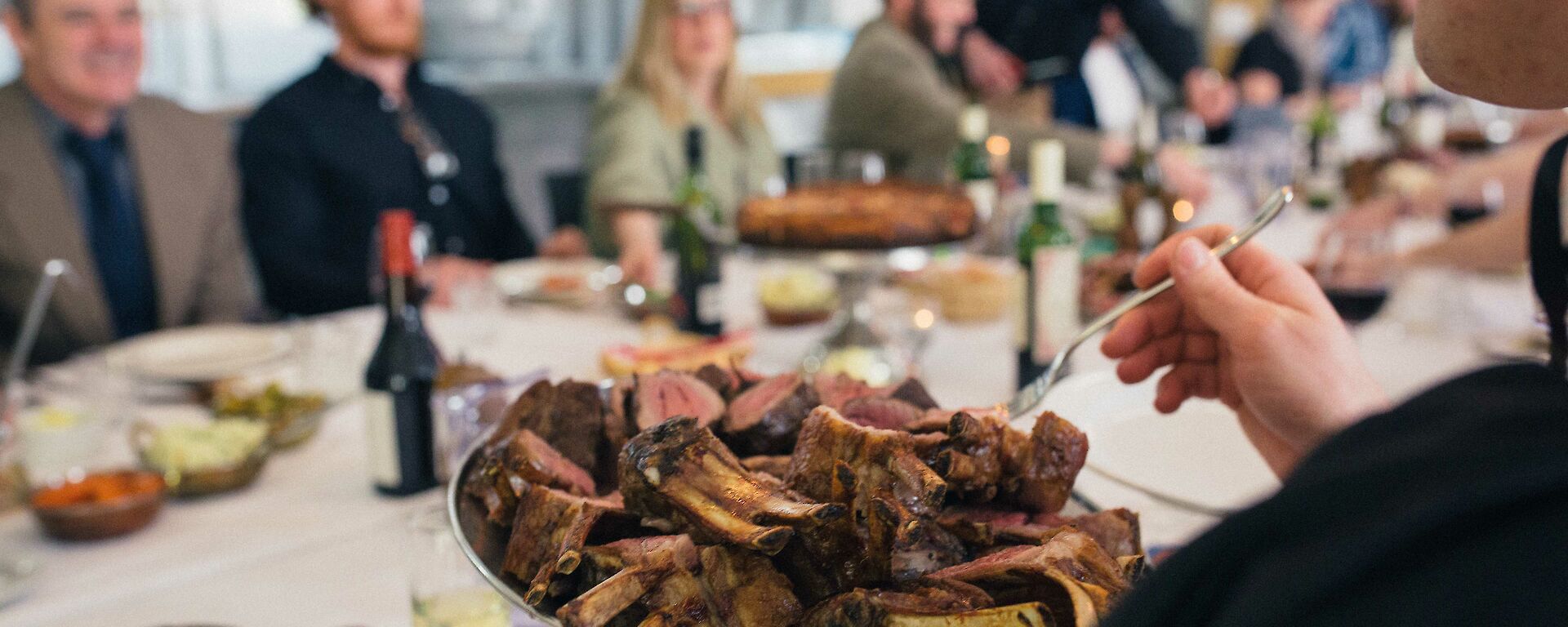 Close up of tray of lamb racks with people at table in background