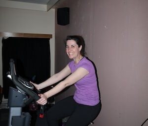 Woman smiling at camera and riding exercise bike in darkened room