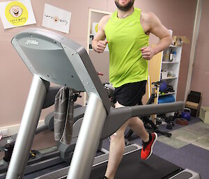 Man in flour singlet, running fast on treadmill, smiles to the camera