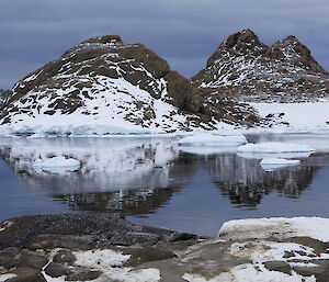 The peaks of two rocky hills reflected in the still waters of a bay