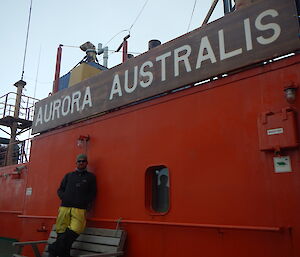 Man stands on upper deck of the icebreaker Aurora Australia, under the large wooden sign