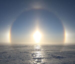 Expanse of flat ice and blue sky above with sun halo centre picture