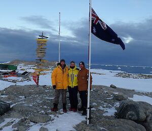 Three people with flag at Casey station for 72nd ANARE