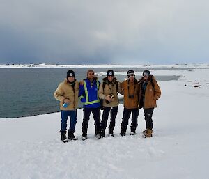 Five expeditioners in a group photo with Newcomb Bay in the background