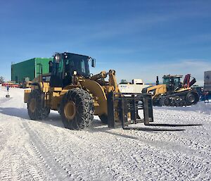 Large forklift moving forward with tracker in the background and the green stores building