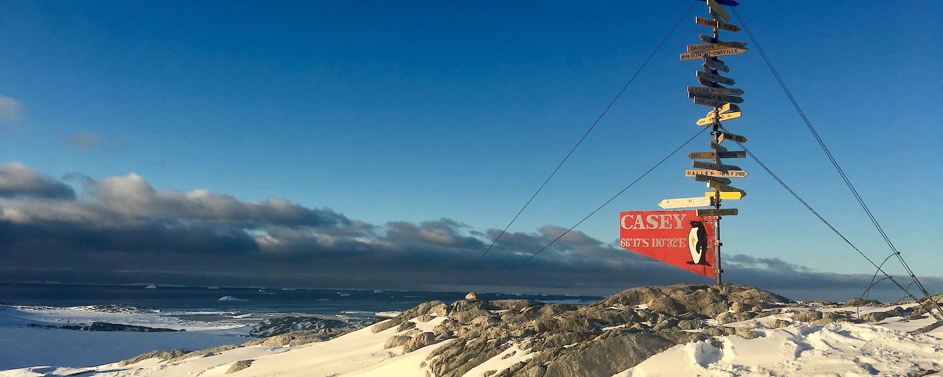 Sunset lighting on the Casey sign post with a background of Newcomb Bay and foreground of snow and rock