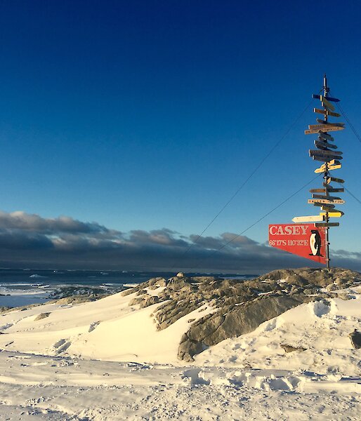 Sunset lighting on the Casey sign post with a background of Newcomb Bay and foreground of snow and rock