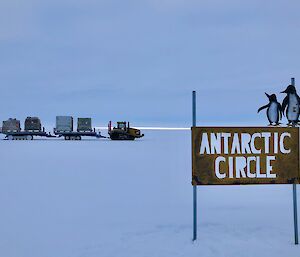 Antarctic Circle sign with a tractor with two pallets being towed carrying four larger containers