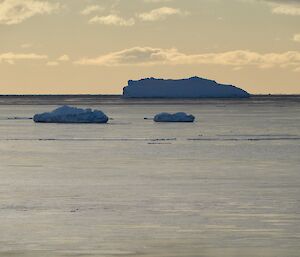 Two smaller icebergs in front a larger iceberg in the distance