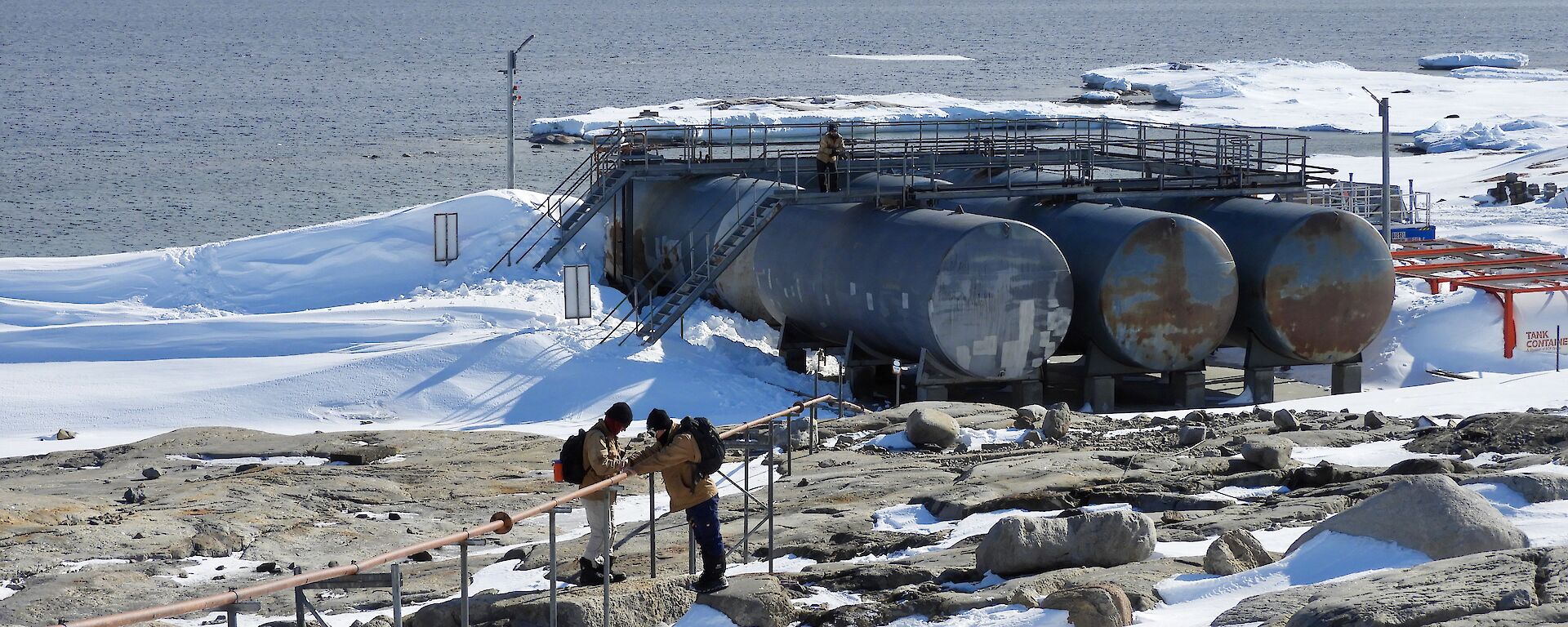Two Casey team members walking the line and one standing on top of the lower fuel farm keeping an eye on fuel transfer operations