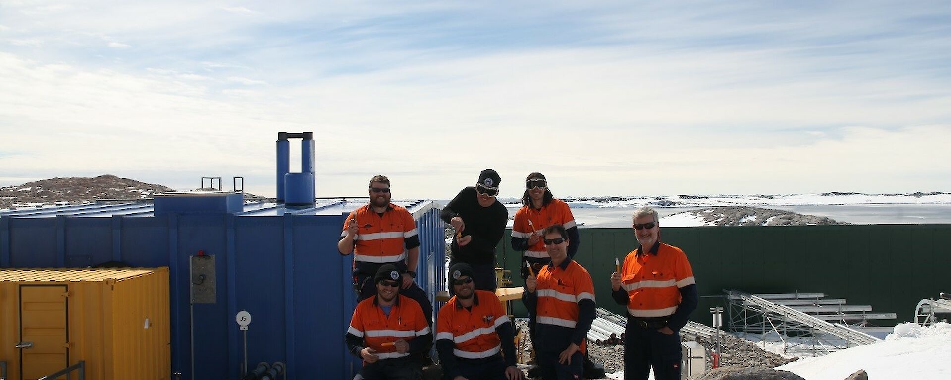 The electrical team standing near the Casey Emergency Power House (EPH, Blue building) with their “magic” test sticks and Newcomb Bay in the background.