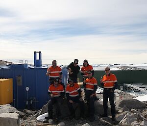 The electrical team standing near the Casey Emergency Power House (EPH, Blue building) with their “magic” test sticks and Newcomb Bay in the background.