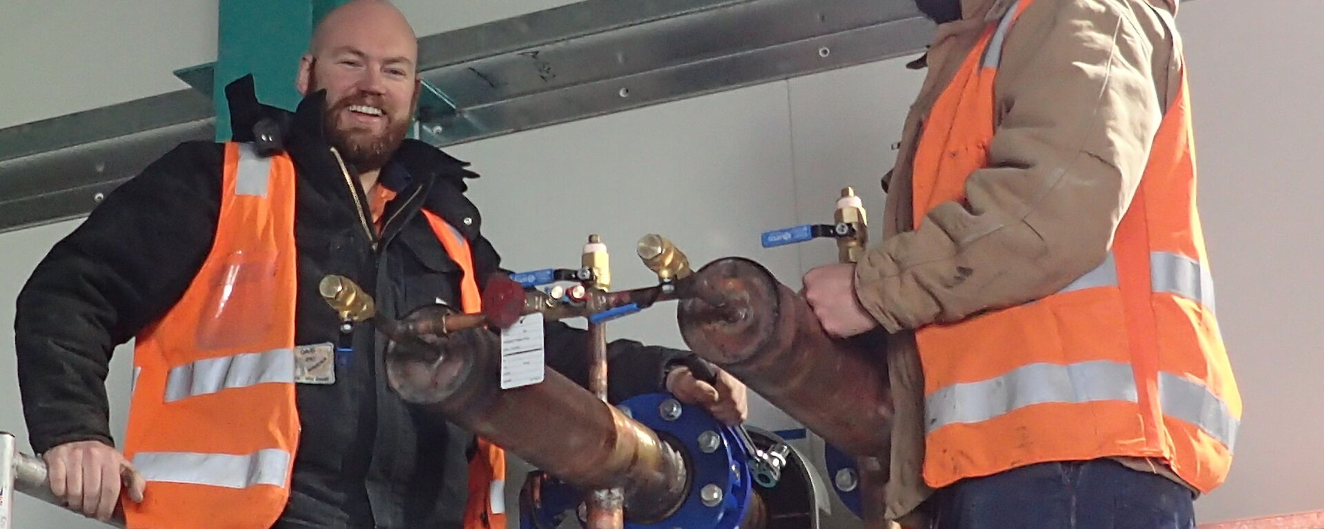 Tradesmen smiling at camera next to internal pipe work