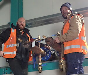 Tradesmen smiling at camera next to internal pipe work