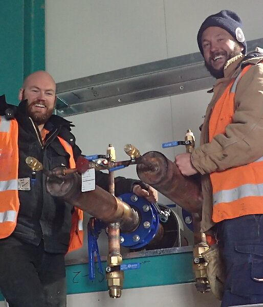 Tradesmen smiling at camera next to internal pipe work
