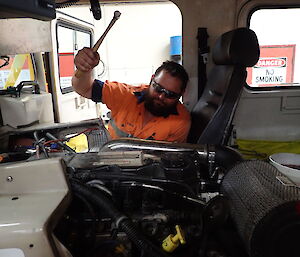 Tradesperson holding a hammer in jest above a vehicle engine