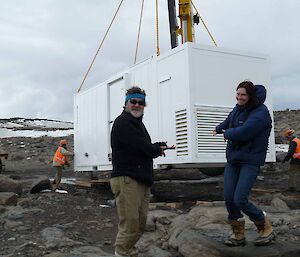 Two expeditioners smiling in foreground. Background installation of a prefabricated lab at Davis