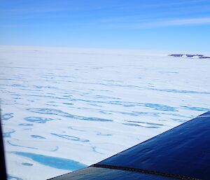 Photo of scenery from aeroplane showing a large lake covered by snow and sea ice on a clear day