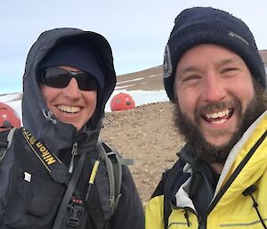 Two expeditioners smiling at camera, huts in background