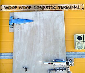 Close up of a wooden door with wooden sign above reading ‘Woop Woop domestic terminal'