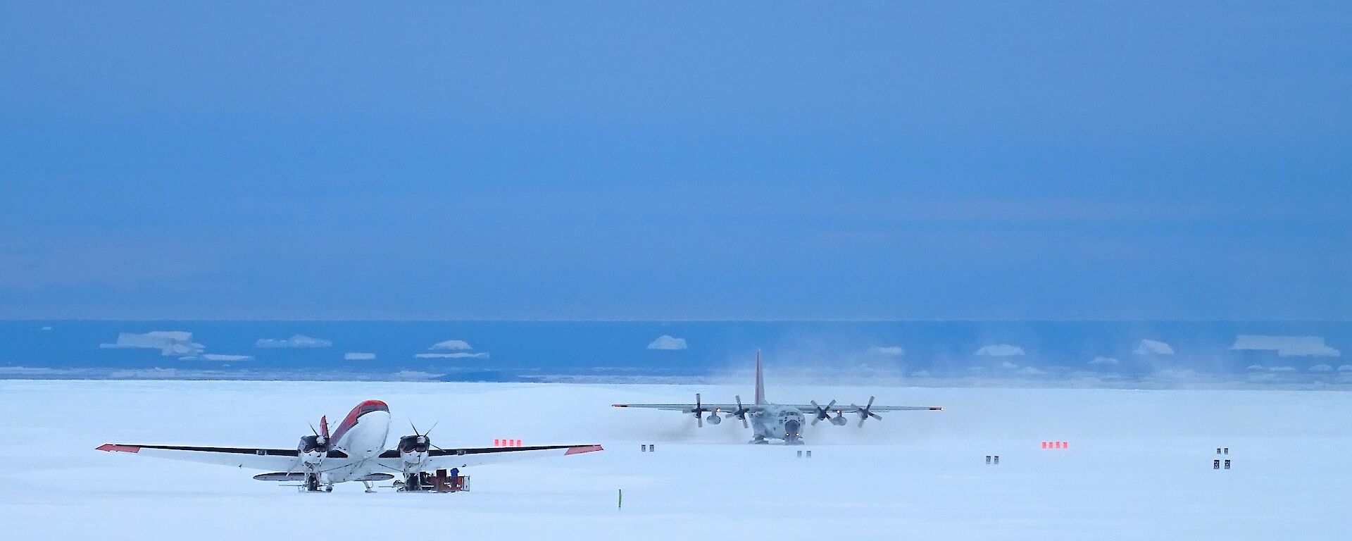 C130 cargo aircraft taxiing past another aircraft on the ski landing area at Davis