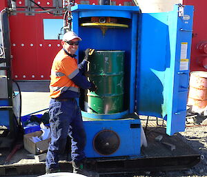 Expeditioner standing in front of a drum crusher with an empty fuel drum