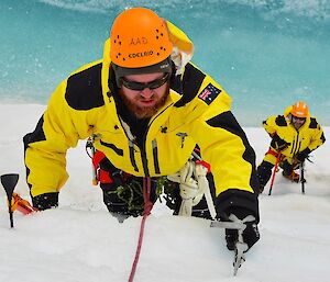 Expeditioner practicing ice climbing up an ice cliff whilst two others look on