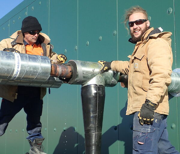 Tradesmen working on a section of pipe into a large green waste treatment building