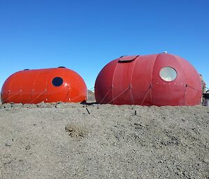 A bright red new hut next to a faded red old hut in a field location